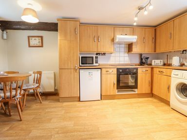 A kitchen with wooden cabinets a microwave oven a washing machine and a dining table with chairs at Llys-y-Wennol in Penmachno