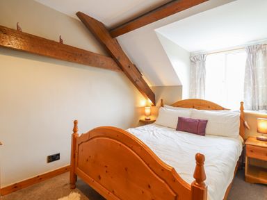 A bedroom with a wooden bed frame bedside tables lamps and visible wooden ceiling beams at Llys-y-Wennol in Penmachno