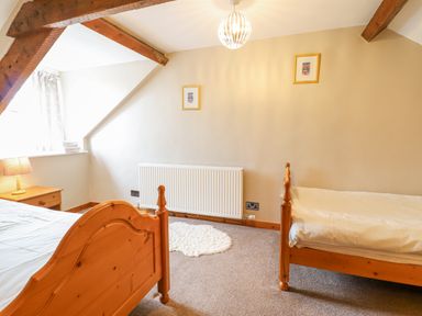 A bedroom with two wooden beds a nightstand with a lamp a window with curtains and two framed pictures on the wall at Llys-y-Wennol in Penmachno