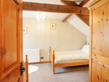 A bedroom with a wooden bed and wardrobe a radiator and exposed wooden beams at Llys-y-Wennol in Penmachno