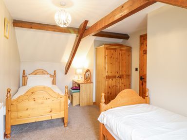 A bedroom with two single wooden beds a wooden wardrobe and a dressing table with a lamp at Llys-y-Wennol Penmachno