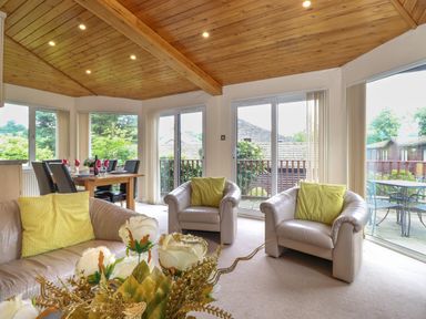 A living room with leather sofas and yellow cushions with a dining table and chairs near large windows at Lodge 3 At Pound Farm Crook near Kendal