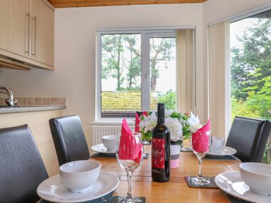 A dining area with a wooden table set with bowls plates wine glasses pink napkins a bottle of mulled wine and a flower centerpiece at Lodge 3 At Pound Farm Crook near Kendal