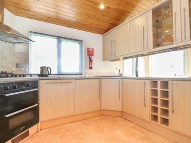 A kitchen with wooden cabinets a gas stove a kettle and a fire extinguisher at Lodge 3 At Pound Farm in Crook near Kendal