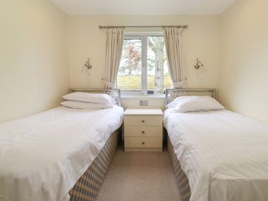 A bedroom with two single beds separated by a three drawer nightstand and a window with curtains at Lodge 3 At Pound Farm Crook near Kendal