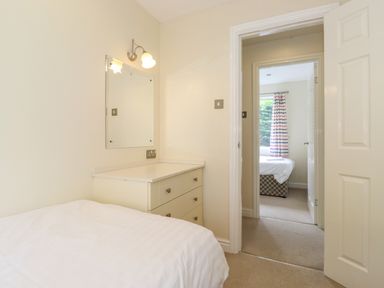 A bedroom with a bed chest of drawers and a wall mirror with a view through an open door to another room with a bed and striped curtains at Lodge 3 At Pound Farm in Crook near Kendal