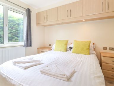 A bedroom with a bed with white sheets and yellow pillows next to two wooden bedside tables and a window with grey curtains at Lodge 3 At Pound Farm Crook near Kendal