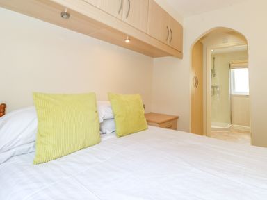 A bedroom with a bed with two green pillows overhead cupboards and a view into a bathroom at Lodge 3 At Pound Farm in Crook near Kendal