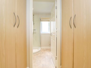 A corridor with wooden wardrobes on both sides leading to a bathroom with a shower and a window at Lodge 3 At Pound Farm in Crook near Kendal