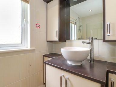 A bathroom with a round white basin on a dark countertop next to a window and cabinets at Lodge 3 At Pound Farm in Crook near Kendal