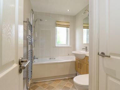 A bathroom with a bathtub shower combination a sink with storage below a window and a towel radiator at Lodge 3 At Pound Farm in Crook near Kendal