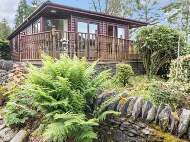 A wooden cabin with a deck surrounded by stone walls and green plants at Lodge 3 At Pound Farm in Crook near Kendal