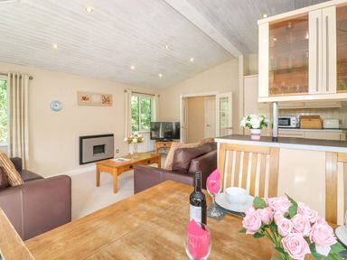 A living room with sofas a wooden coffee table and a dining table with flowers and wine bottle at Lodge 7 At Pound Farm in Crook near Kendal