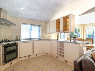 A kitchen with white cabinets a gas stove a kettle a window and a dining area with chairs and a table at Lodge 7 At Pound Farm in Crook near Kendal