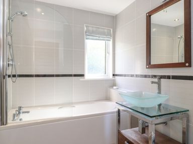 A bathroom with a bathtub shower combo a frosted window a glass vessel sink on a metal and wood vanity and a mirror on the wall at Lodge 7 At Pound Farm Crook near Kendal
