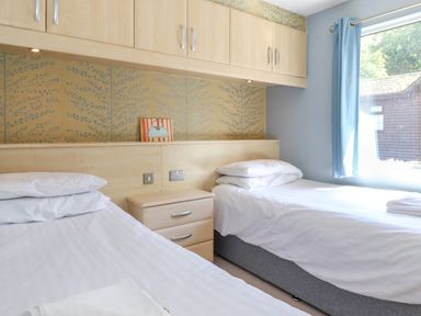 A bedroom with two single beds separated by a bedside table and a window with blue curtains at Lodge 7 At Pound Farm in Crook near Kendal