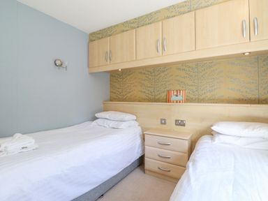 A bedroom with two single beds a bedside table and overhead cabinets at Lodge 7 At Pound Farm in Crook near Kendal