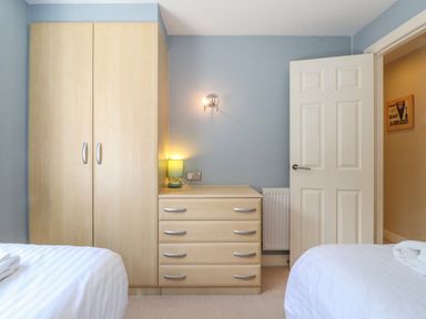 A bedroom with two beds a wooden wardrobe a chest of drawers with a lamp and an open door at Lodge 7 At Pound Farm in Crook near Kendal