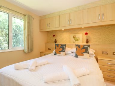 A bedroom with a double bed white linens rolled towels cushions window and overhead cabinets at Lodge 7 At Pound Farm Crook near Kendal