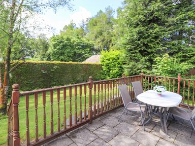An outdoor patio with a table and four chairs overlooking a garden with trees and hedges at Lodge 7 At Pound Farm in Crook near Kendal