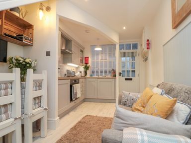 A kitchen and living area with cabinets chairs sofa with pillows and a door at Little Gem in Whitby