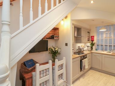 A kitchen with wooden countertops and gray cabinets next to a small dining area under a staircase at Little Gem in Whitby