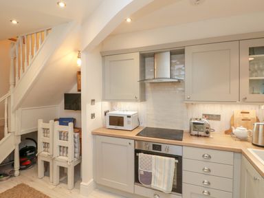 A kitchen with grey cabinets a microwave toaster kettle and oven under a staircase at Little Gem in Whitby