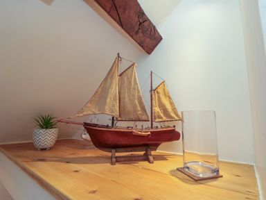 A wooden model sailboat on a wooden shelf with a small potted plant and a clear glass vase at Little Gem in Whitby