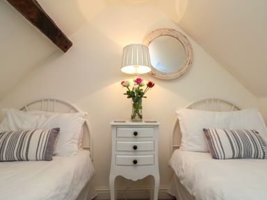 A bedroom with two single beds a bedside table with a lamp and flowers and a round mirror on the wall at Little Gem in Whitby