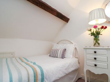 A bedroom with a single bed a striped pillow a bedside table with a lamp and flowers at Little Gem in Whitby