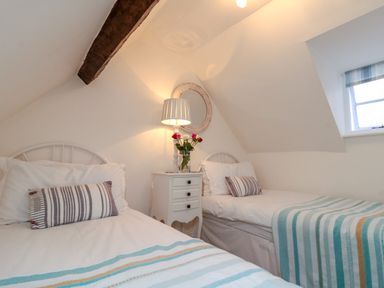 A bedroom with two single beds a white nightstand with a lamp and flowers under a slanted ceiling at Little Gem in Whitby