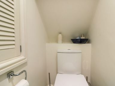 A small bathroom with a toilet paper holder a toilet and shelves with bathroom items at Little Gem in Whitby
