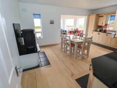 A dining area with a white table and chairs next to a kitchen with wooden cabinets and a black stove in a house at Cois Leice Cushlecka near Mulranny County Mayo