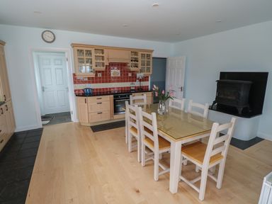 A kitchen with wooden cabinets a red tiled backsplash a glass top dining table with six chairs and a wood stove at Cois Leice Cushlecka near Mulranny County Mayo