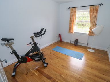 A room with an exercise bike a blue yoga mat a white floor lamp and a window with orange curtains at Cois Leice Cushlecka near Mulranny County Mayo