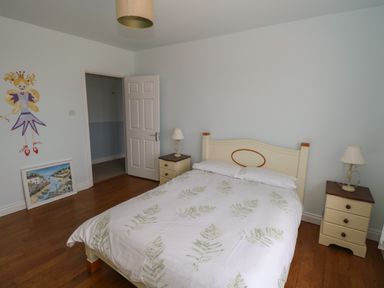A bedroom with a bed and two bedside tables with lamps and a wall painting and a framed picture on the floor at Cois Leice in Cushlecka near Mulranny County Mayo