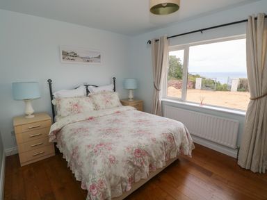 A bedroom with a bed with floral bedding two bedside tables with lamps and a large window overlooking a gate and ocean at Cois Leice in Cushlecka near Mulranny County Mayo