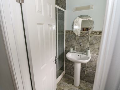 A bathroom with a pedestal sink a round mirror and a partially open door at Cois Leice in Cushlecka near Mulranny County Mayo
