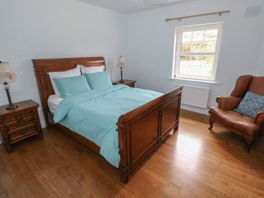 A bedroom with a wooden bed with blue bedding two wooden nightstands with lamps a window and a brown armchair at Cois Leice Cushlecka near Mulranny County Mayo