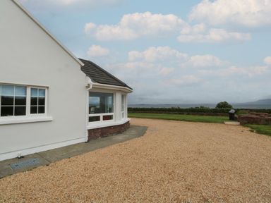 The side of a white house with windows a gravel driveway and a lawn with a view of the sea and cloudy sky at Cois Leice Cushlecka near Mulranny County Mayo
