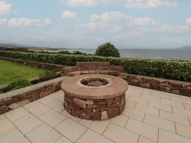 An outdoor patio area with a stone fire pit and curved stone bench overlooking the sea at Cois Leice Cushlecka near Mulranny County Mayo