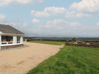 A gravel driveway next to a house with grass and stone walls overlooking a body of water at Cois Leice in Cushlecka near Mulranny County Mayo