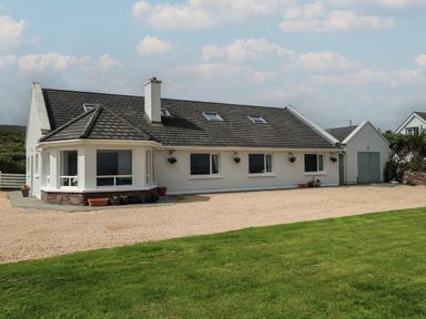 A single story house with a pitched roof and attached garage surrounded by gravel and lawn at Cois Leice in Cushlecka near Mulranny County Mayo