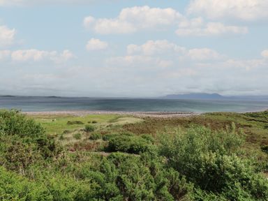 A coastal landscape with green vegetation a rocky shoreline and sea with distant hills at Cois Leice in Cushlecka near Mulranny County Mayo