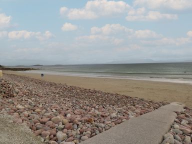 A beach with a rocky shoreline and sandy area beside calm sea and cloudy sky at Cois Leice in Cushlecka near Mulranny County Mayo