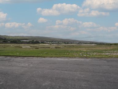 A rural landscape with grassy fields and scattered rocks under a partly cloudy sky in Cois Leice Cushlecka near Mulranny County Mayo