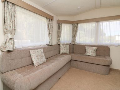An L shaped sofa with floral cushions in a room with corner windows and floral curtains at 23 Manleigh Park in Combe Martin