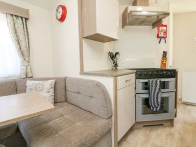 A kitchen area with an oven stove a corner bench seat with a cushion and a table at 23 Manleigh Park in Combe Martin
