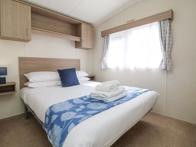 A bedroom with a double bed with white linens and blue accents at 23 Manleigh Park in Combe Martin