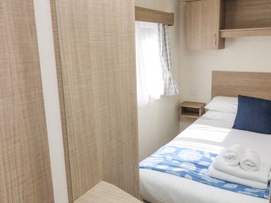 A small bedroom with a single bed with folded towels and a pillow next to a window with curtains at 23 Manleigh Park in Combe Martin